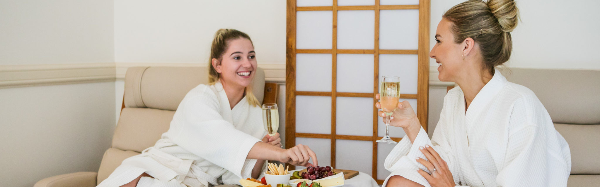 Two women talking to each other while eating fruits and drinking champagne